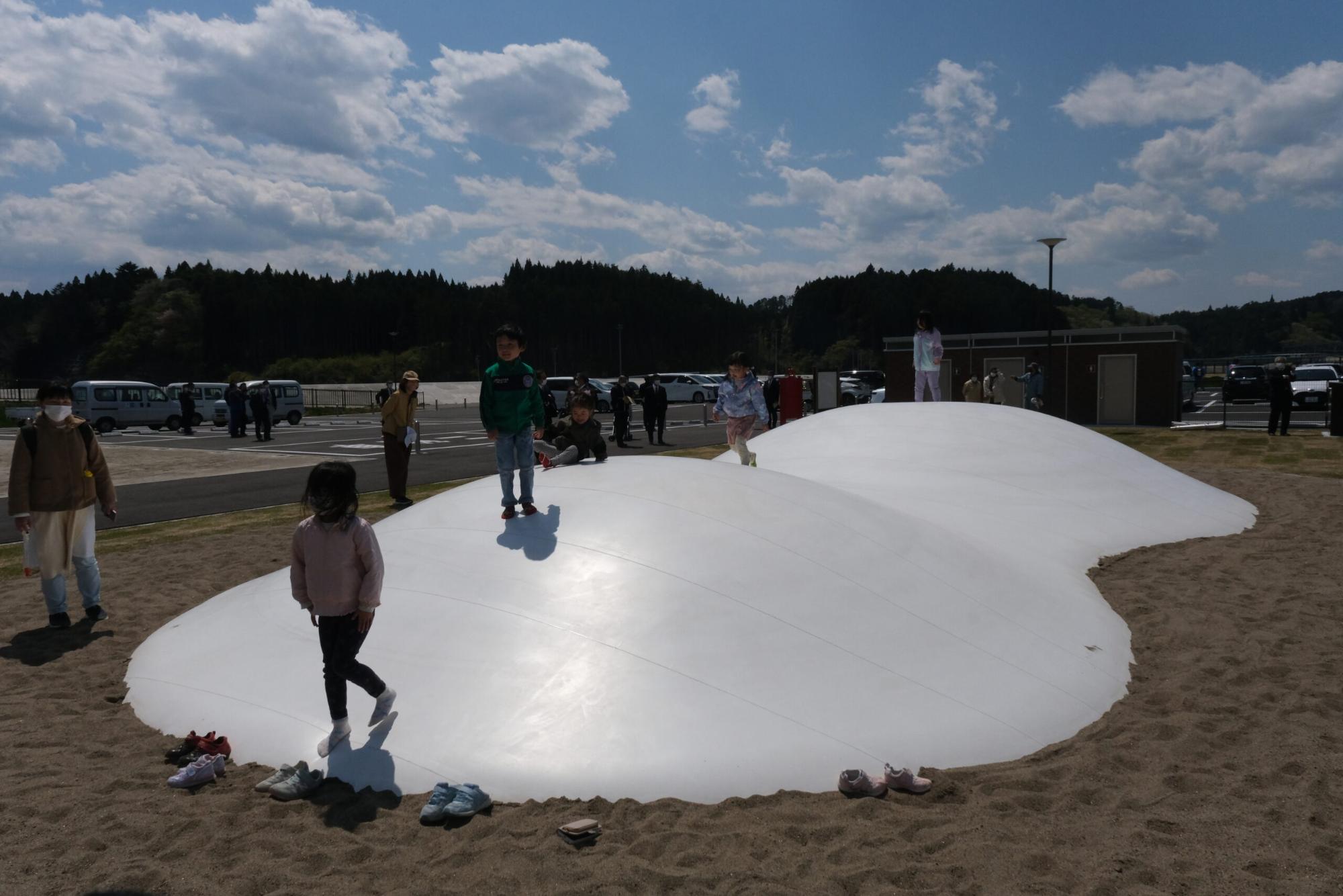 2つの山がある白いドーム型の遊具の上で、子どもたちが裸足で跳ねたり歩いたりして遊んでいる写真