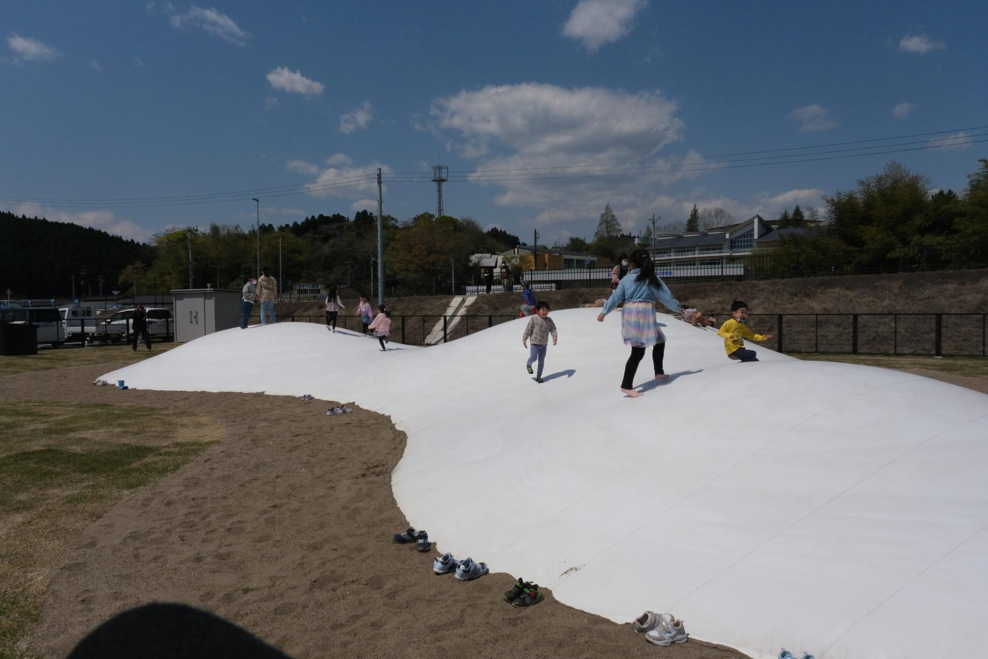 3つの山がある白いドームの上で、多くの子どもたちが元気に飛び跳ねている様子の写真