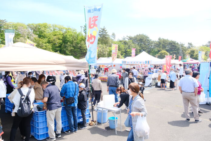 屋外で開催されている南三陸町の「潮騒まつり」の会場に、多くの来場者が集まり、ホヤや海産物などを扱う露店が立ち並び賑わっている様子の写真
