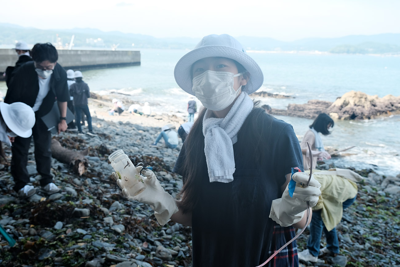 女の子が手袋をつけ、拾ったごみ（瓶や紐のようなもの）を見せている写真