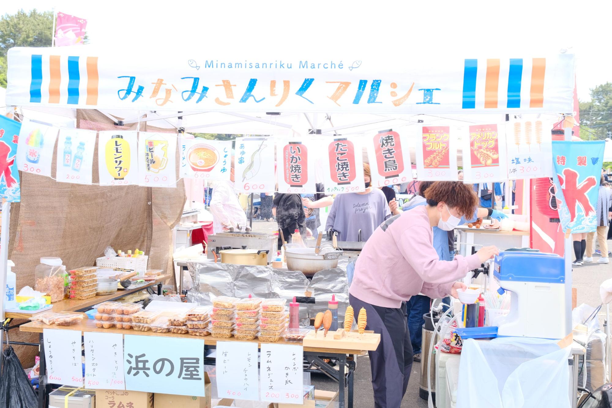 「みなみさんりくマルシェ」の看板が掲げられた屋台で、かき氷を作っている男性の手前には、パック詰めされた料理などが並んでいる写真