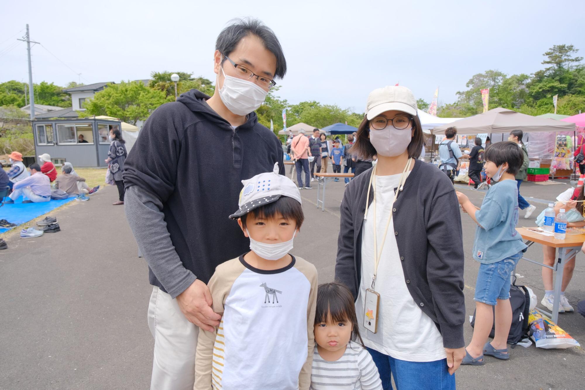屋外のイベント会場で、家族4人がマスクを着けてカメラに向かって立っている写真