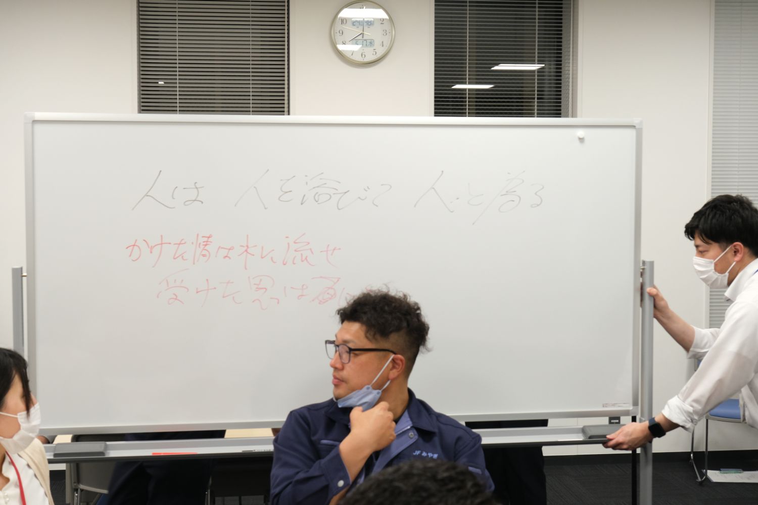「人は人を浴びて人に為る」という文字が書かれたホワイトボードを男性が動かし、その前では参加者たちが話し合っている様子の写真