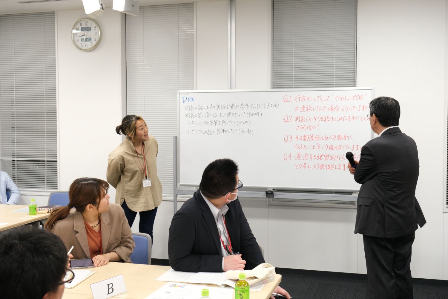 文章が書かれたホワイトボードの右横にマイクを持った塾長が立ち、席に着いた参加者たちもホワイトボードの方を向いている様子の写真
