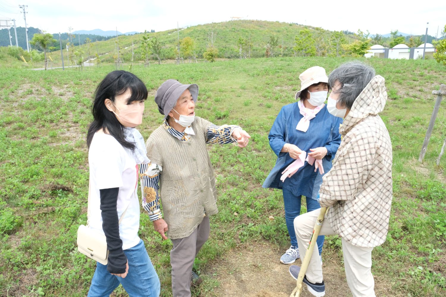 数人の女性たちが草地で立ち話をしており、そのうちの一人が指をさして何かを説明している様子の写真