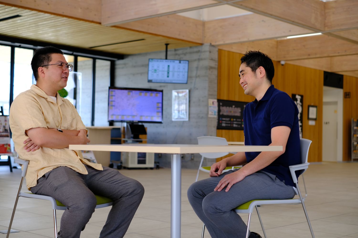二人の男性が明るい室内で向かい合って座り、楽しそうに会話している写真