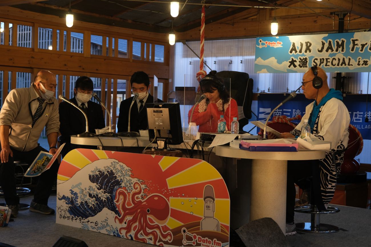 志津川高校の皆さんがラジオブースに集まり、マイクの前で会話をしている様子の写真