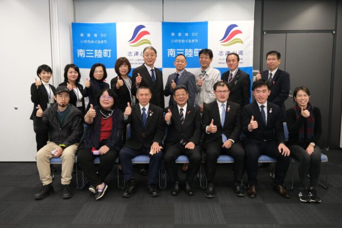 台北市の防災関連職員6名と南三陸町の町長および関係者が2列に並び、全員が親指を立てたポーズでカメラに向かって笑顔を見せている集合写真