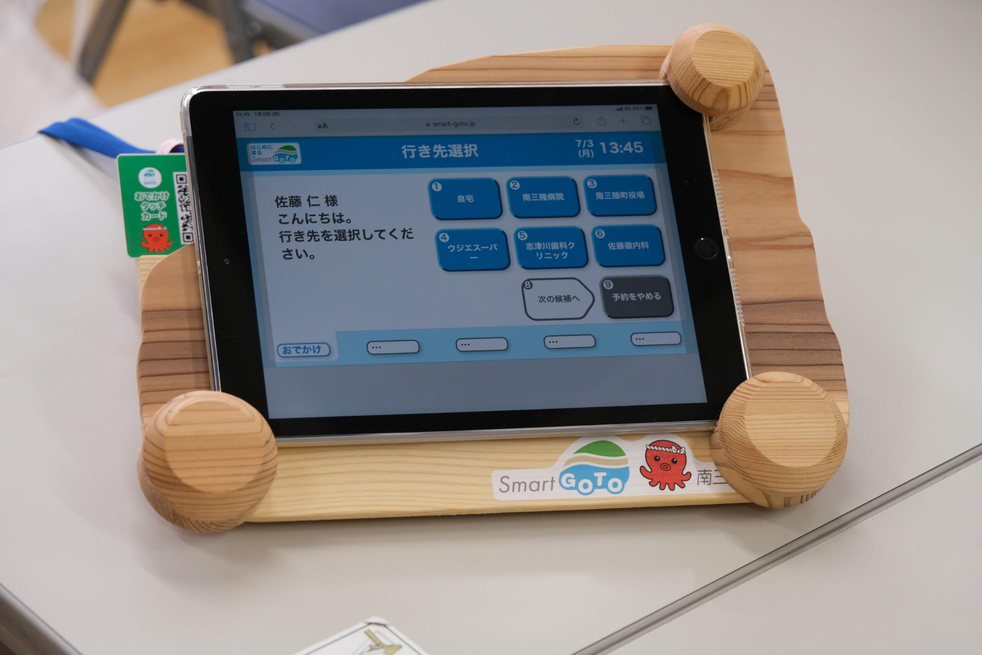 タブレットが木製のスタンドに置かれており、画面には「行き先選択」と表示されたメニューが映っている写真