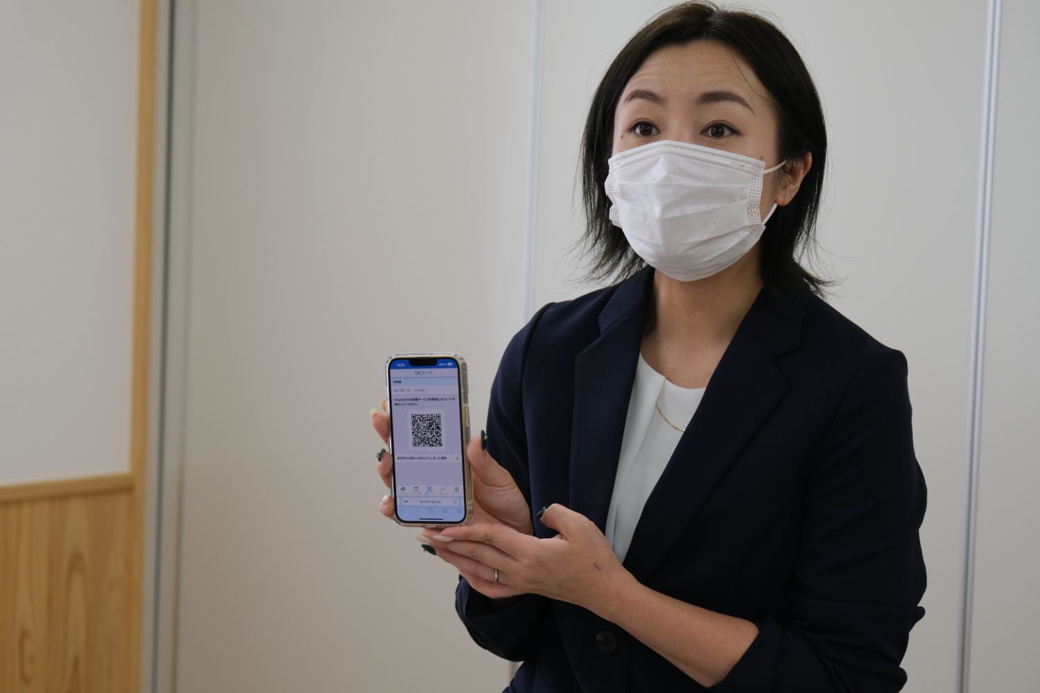 黒いジャケットを着た女性がスマートフォンを持ち、画面にはQRコードが表示されている写真