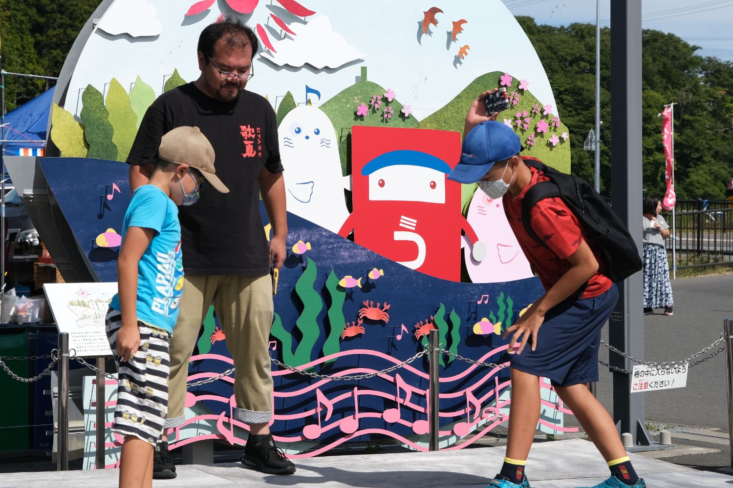 大人が見守る中、子どもたちがキャラクターのパネルの前で遊びながら交流している地域の子ども向けイベントの写真