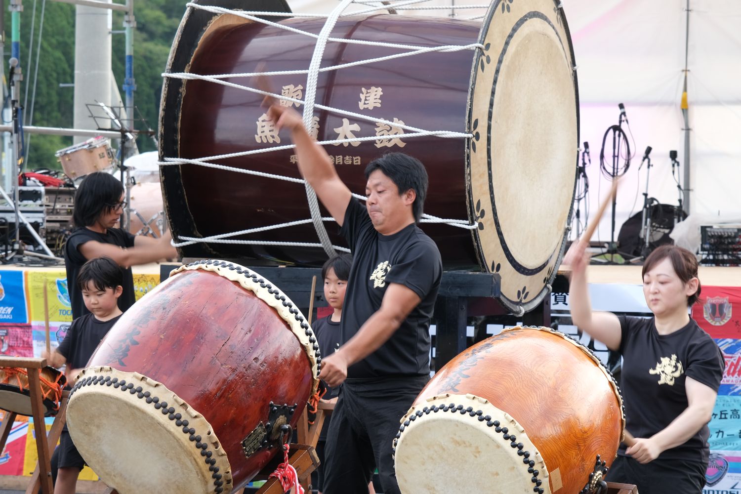 黒いTシャツを着た参加者たちが大きな和太鼓を叩いている様子の写真