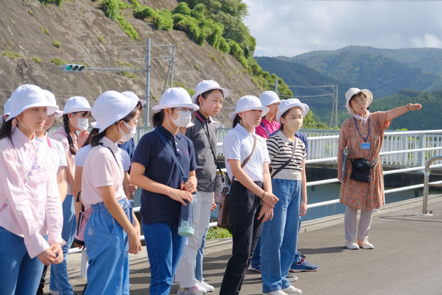 屋外で白い帽子をかぶり、マスクを着用した子どもたちが指導を受ける様子の写真