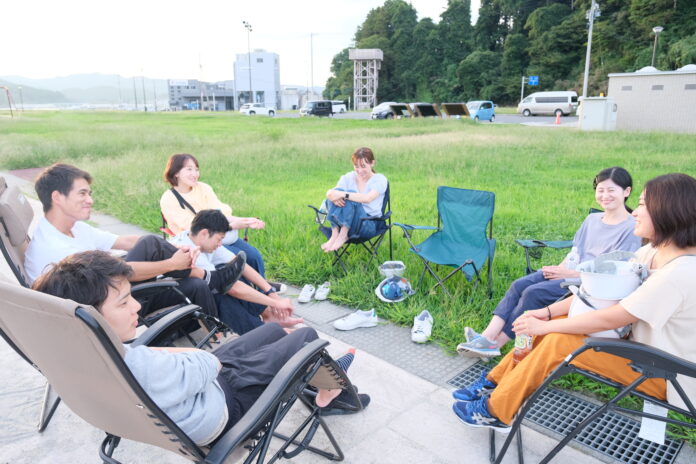 参加者たちが芝生広場でリクライニングチェアに座りながら談笑し、リラックスした雰囲気で交流している様子の写真