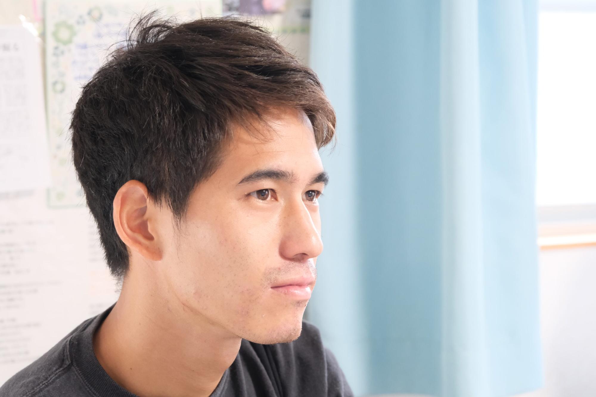 明るい室内で、若い男性が真剣なまなざしで前方を見つめている田島聡士さんの写真