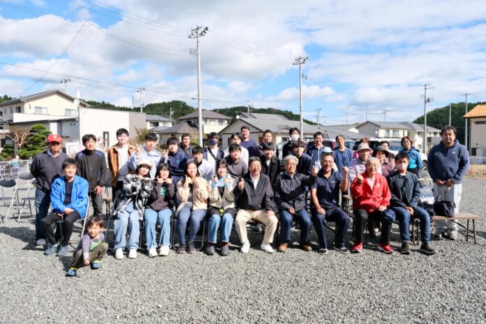 晴れた空の下、住宅街の一角で開かれた交流イベントに集まった地元住民と高校生たちが、屋外で並んで記念写真