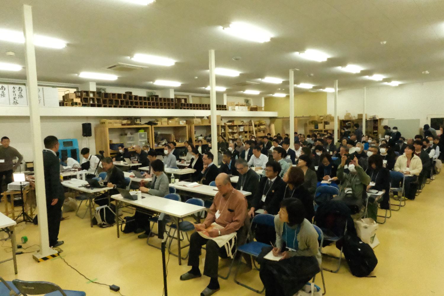 多くの参加者がテーブルに座ってノートを取りながら講師の説明を聞いている研修会の様子の写真