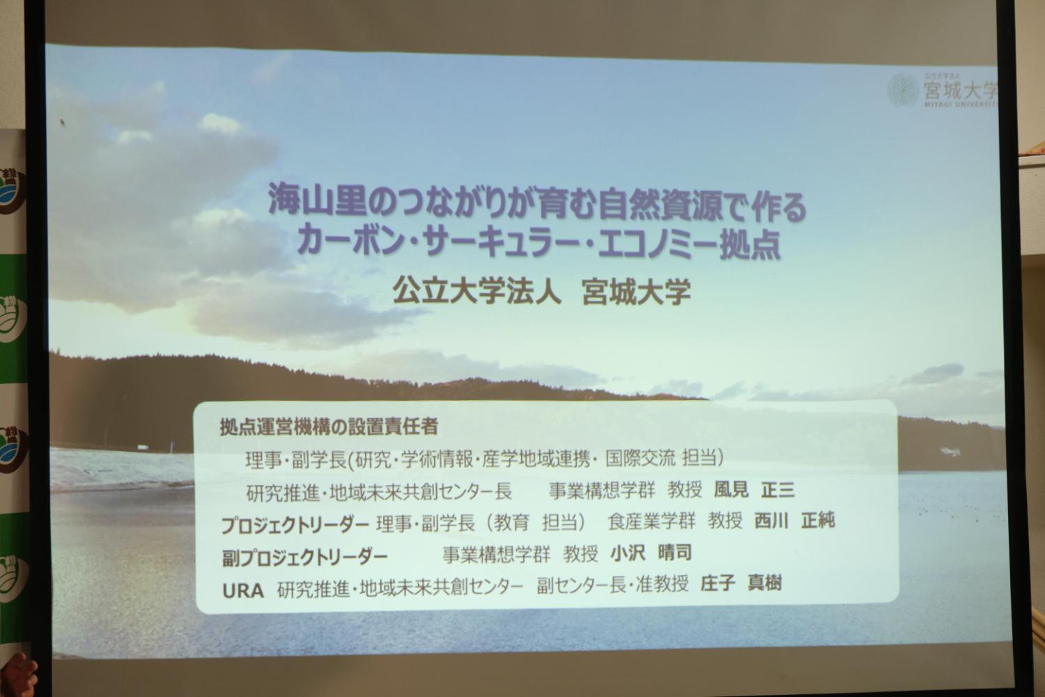 海の風景写真を背景に海山里のつながりが育む自然資源で作るカーボン・サーキュラー・エコノミーの拠点と書かれ宮城大学、設置責任者、プロジェクトリーダーなど記されたスクリーン画面の写真