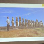 青空の下で乾いた赤土の大地で一列に並んだ15体のモアイ像と一緒に左側に男性が同じ方向を見て立っている写真（DSCF9458のページへリンク）