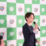 宮城大学のロゴが入った緑と白のチェック柄のパネルの前に黒いスーツを着た女性が右手にマイクを持ち、話をしている写真（DSCF9465のページへリンク）