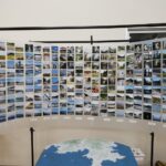 たくさんの風景や場所の写真が横長にカード状に並べられカーブを描くように展示され、その前に地形の模型が置かれている展示物の写真（DSCF9552のページへリンク）