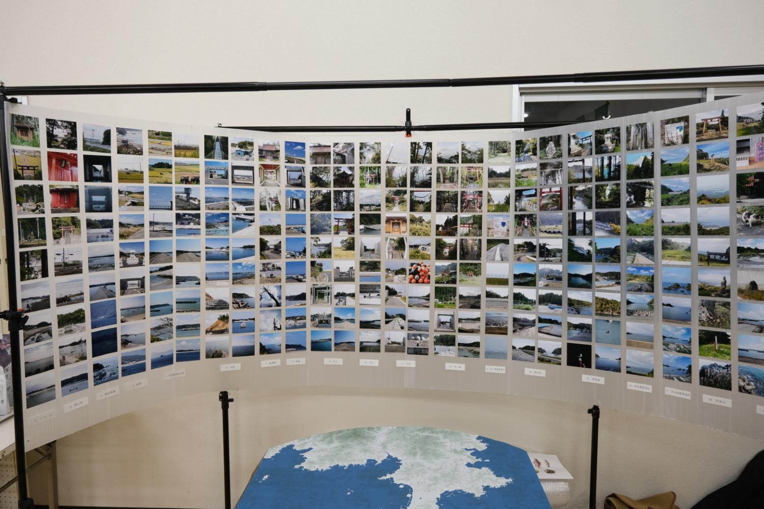 たくさんの風景や場所の写真が横長にカード状に並べられカーブを描くように展示され、その前に地形の模型が置かれている展示物の写真