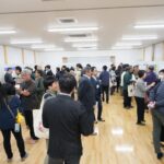 室内の壁際全体にボードが置かれ多くの人々がボードに貼られた掲示物を見ている写真（DSCF9557のページへリンク）