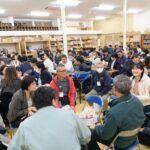 多数の人々が室内の会場で四角形のテーブルを囲んだり、椅子を寄せ円の形にしたグループごとに座って真剣に話し合いや交流をしている様子が写された写真（DSCF9582のページへリンク）