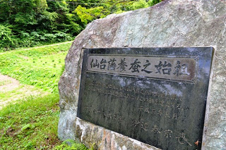 大きな石に黒い銅板が取り付けられ、「仙台藩養蚕之始祖」と彫られた碑文が刻まれている石碑の写真