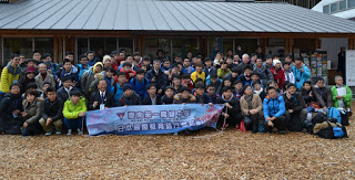 平屋の建物の前に大勢の学生たちと引率の先生や住民たちが集まり、最前列の学生たちが中国語で書かれた横断幕を持っている集合写真