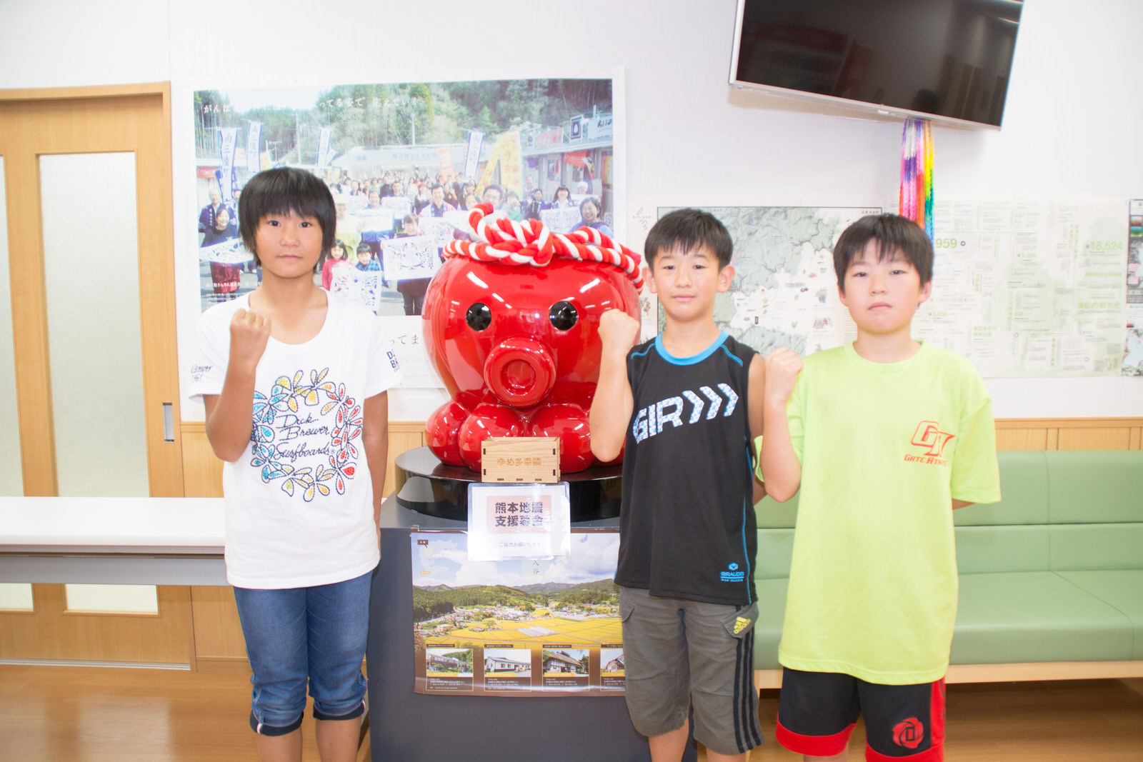 ねじり鉢巻きを巻いた大きな赤いタコの像をはさんで女子児童1人と男子児童2人が並んで立ち、右手でガッツポーズをしている写真