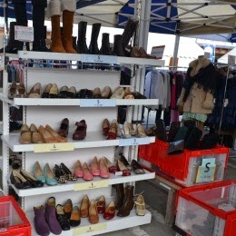 靴やブーツがサイズ別に陳列棚に並べられ、足元に赤いコンテナが置かれている屋外店舗の写真