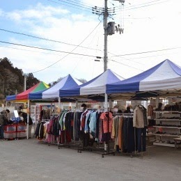 青と白のテントが数張り並び、色とりどりの古着がハンガーラックにかけられている屋外マーケットの写真