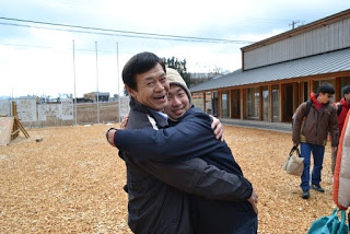 お屋外のスペースで笑顔で抱き合う男性と男子学生の写真