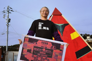 ピラミッドの建物の前で、ボードを持って立つ新井さんの写真