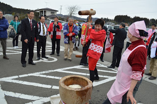 たくさんの人が見守る中、赤い法被を着た女性が杵を振り下ろそうとしている写真