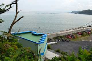 護岸工事がされた海岸沿いに薄いグリーンに青のアクセントが入った建物が建っている写真