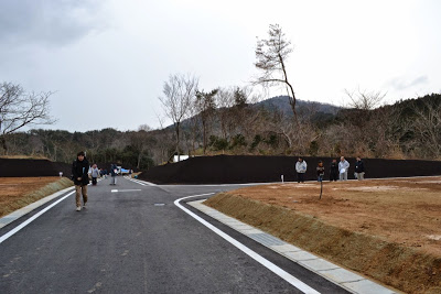 真っすぐに伸びる舗装道路に沿って造成した区画が並び、人々が道路を歩いて見学している様子の写真