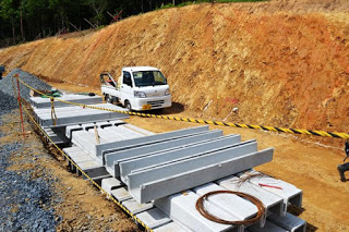 斜面の土がむき出しになっていて、その横にコンクリート製の排水溝の部材が並べられており、工事用の軽トラックが置かれている排水溝の整備作業現場の写真