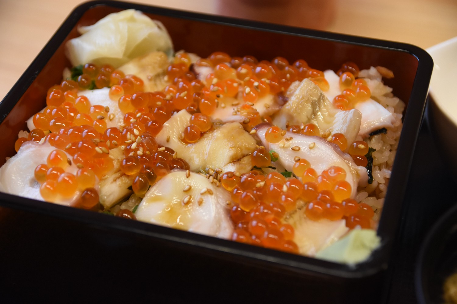 重箱の中にイクラとタコ、あなごがごはんの上に敷き詰められ、白ごまがふりかけられている「さんこめし」のアップ写真