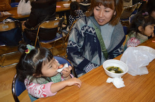 テーブル席に座った親子連れの前にわかめ湯餅が入った白いお椀が置かれており、女の子がいちご大福をほおばっている写真