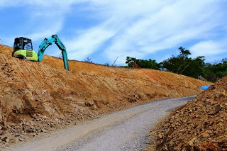 小型のショベルカーが斜面を削って道を広げている様子で、道路や法面を整えている最中の掘削作業中の写真