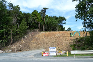 森林の斜面を切り開いて整地し、重機が作業中の造成工事現場の写真