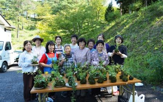 完成したたくさんの苔玉をテーブルに並べ、作業を終えた笑顔の女性たち十数名が一緒に記念撮影している写真