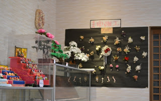 壁沿いにアクリルケースに入った小さいひな壇や、様々なまゆ細工が展示されている写真