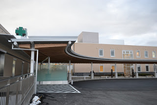 ベージュ色の壁の前にカーブを描いた屋根付きの通路がある病院の写真