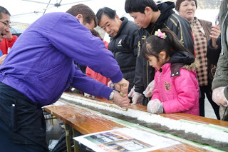参加者の方々が見守る中、海苔の上に広げられたごはんの上にめかぶ納豆を一直線に引いている様子の写真
