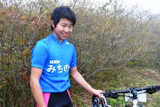 マウンテンバイクの横に立つ青い上着を着た目黒太規さんの写真