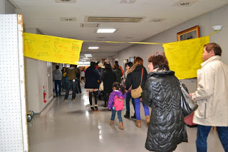 メッセージが書かれた黄色い布が下げられた廊下を、多くの来場者が会場へ向かって歩いている様子を写した写真