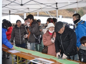 テントの下で、参加者の皆さんが談笑しながら海苔巻きを食べている様子を写した写真